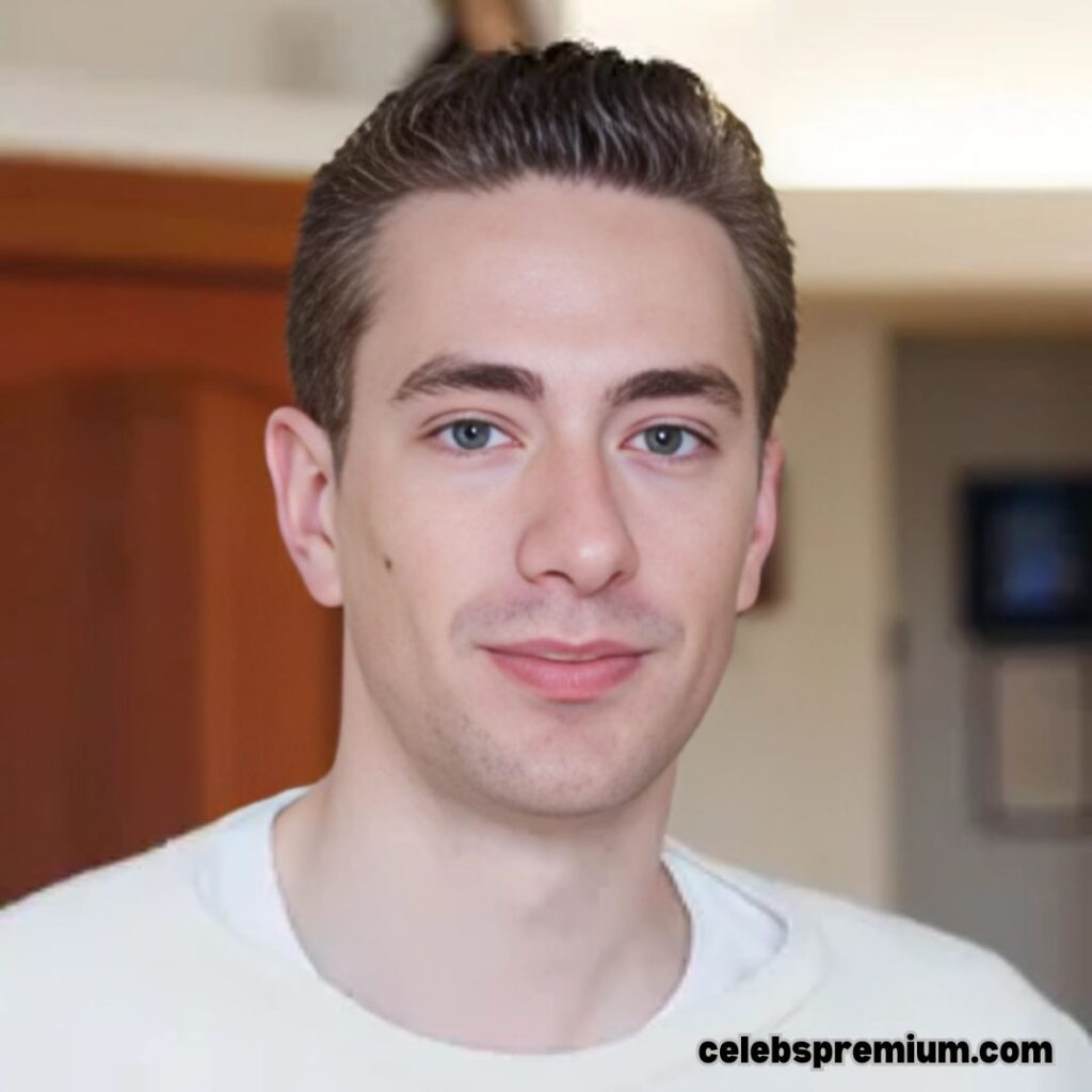 Portrait of Andrew Wilkinson, focusing on his face. He has light blue eyes and short, dark hair. He is wearing a white t-shirt and has a subtle smile.
