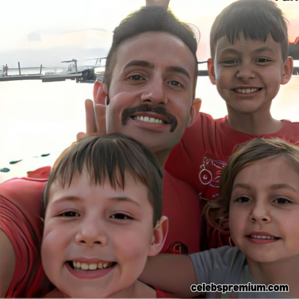 Steve Hamilton is taking a selfie with three smiling children. He is wearing a red shirt, has a mustache, and appears to be enjoying time with the kids.