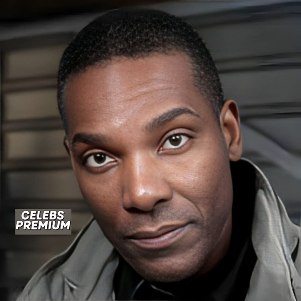 A close-up portrait of Ray Campbell looking directly at the camera with a slight smile. He has short, dark hair and is wearing a light grey jacket over a dark shirt.