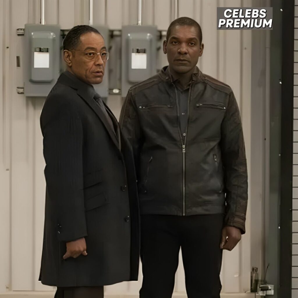 Ray Campbell, wearing a black leather jacket, stands next to Giancarlo Esposito who is wearing a black coat.