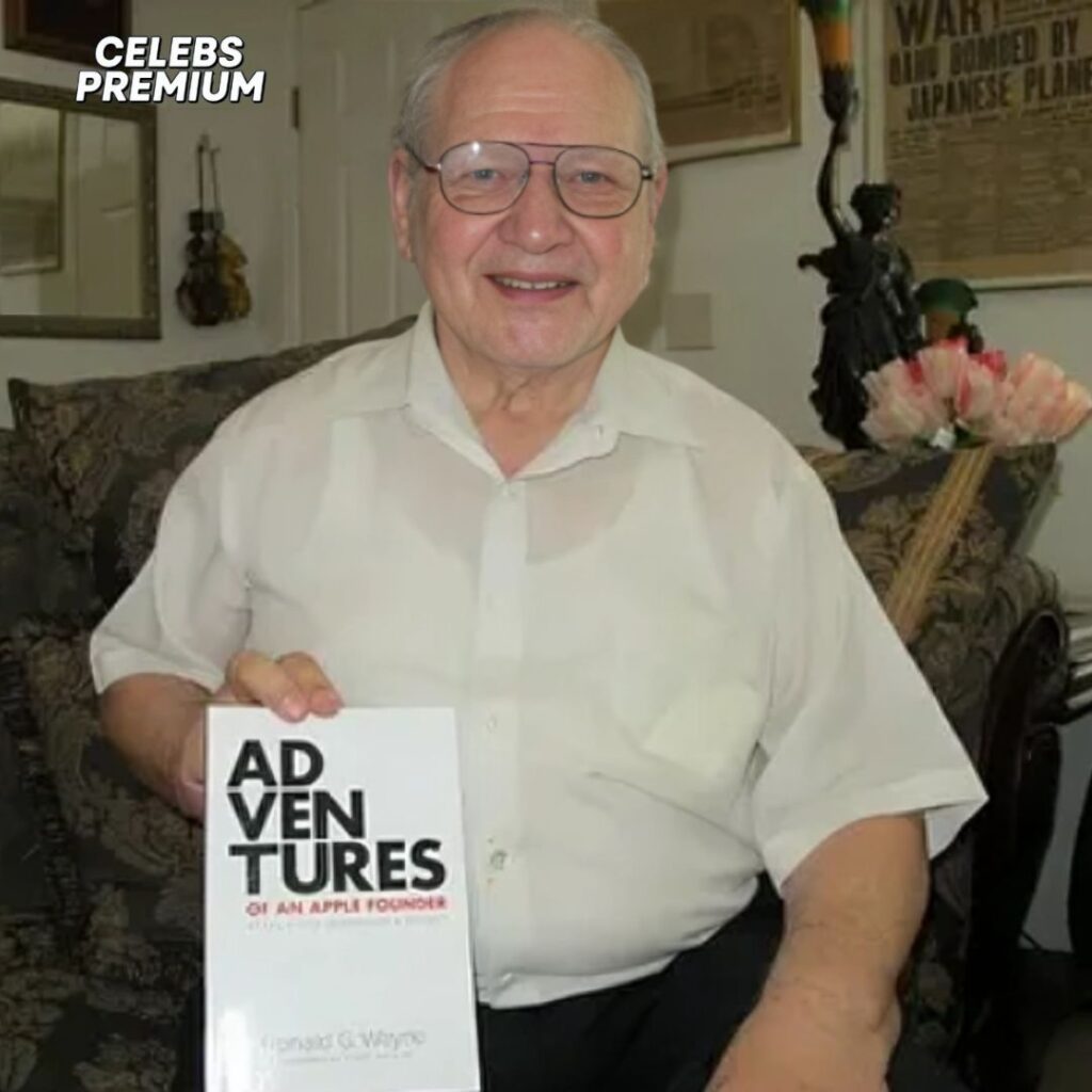 A photo of Ronald Wayne, wearing glasses and a light-colored shirt, sitting in a chair and holding his book, "Adventures of an Apple Founder." The background shows a decorated room.