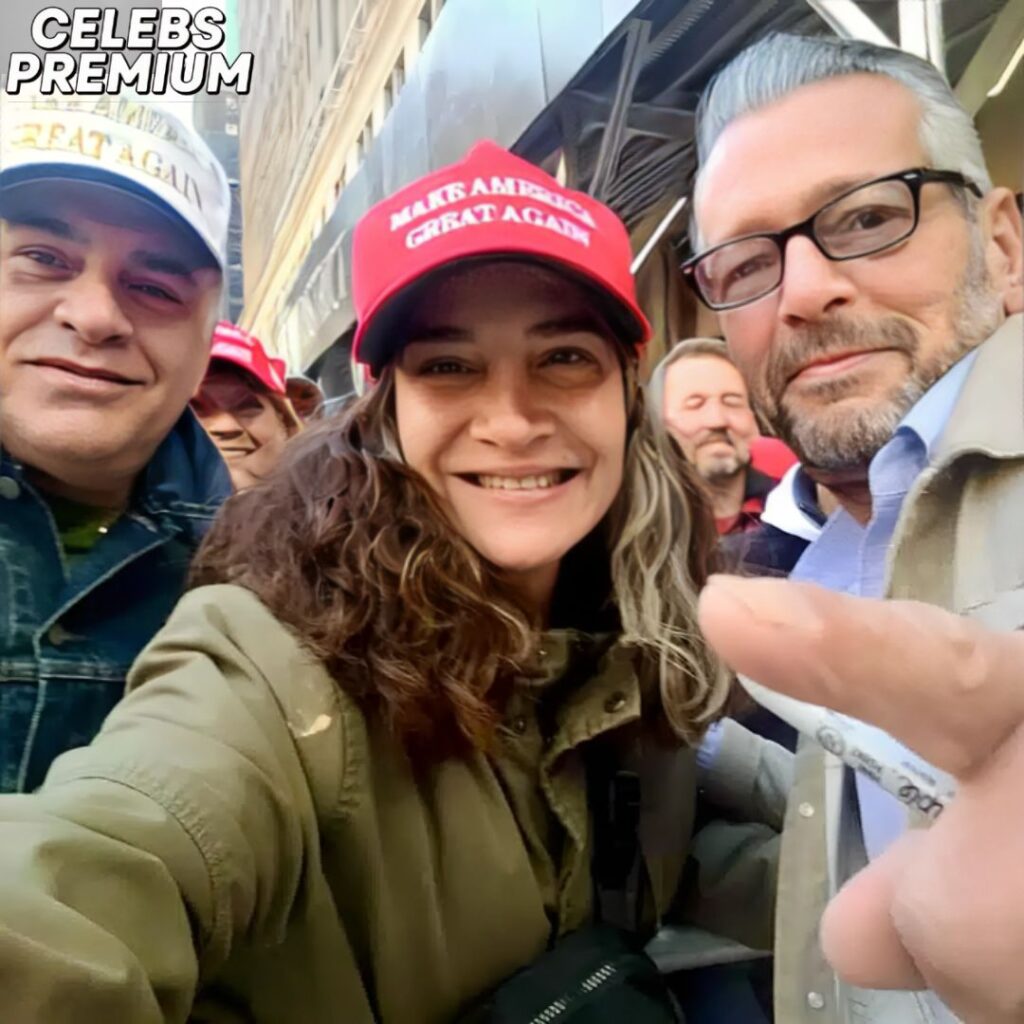 Scott LoBaido is on the right, wearing glasses and a light-colored jacket over a patterned shirt. His friend is on the left, wearing a white cap and a black jacket. They are outdoors. A woman wearing a red cap is in the background.